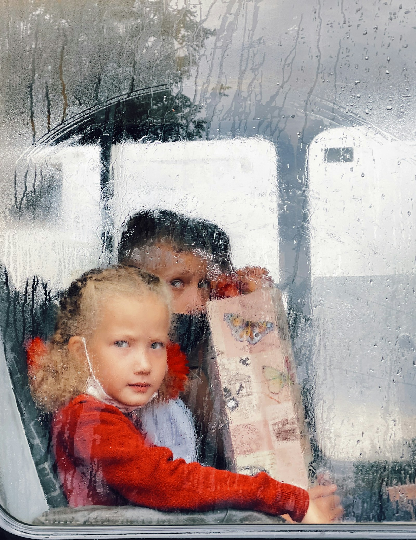 Preschooler in a hat watching rain from a window indoors